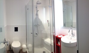 A modern bathroom with a glass-enclosed shower, a white toilet, and a red vanity with a sink. - Campushotel GmbH (Hagen)