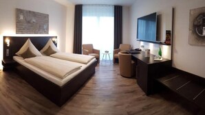 A hotel room with a double bed, a desk, a chair, a TV, and a window with curtains. - Campushotel GmbH (Hagen)