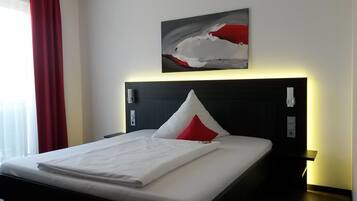 A neatly made bed with white bedding and a red accent pillow, a modern headboard with integrated controls, and a contemporary abstract painting above the bed.