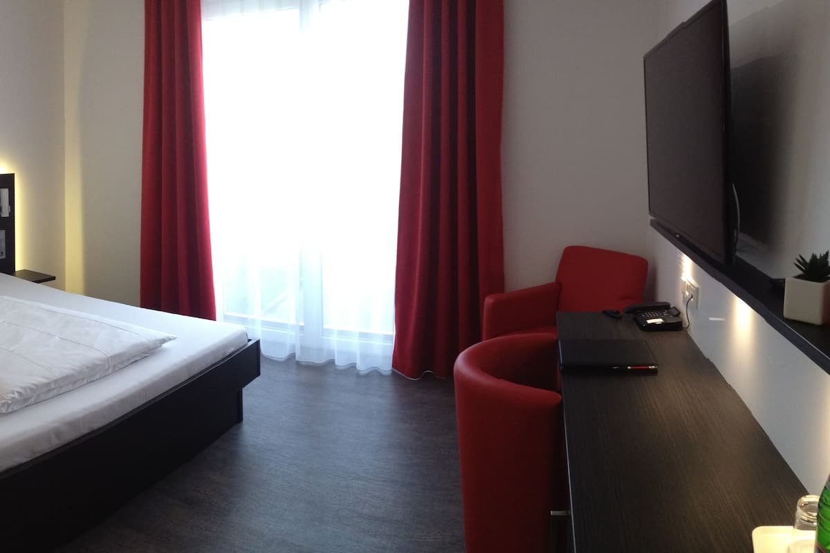 A hotel room with a bed, a desk, a TV, and a red chair.