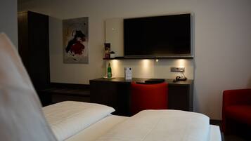 Ein Hotelzimmer mit Bett, Schreibtisch, Stuhl, Fernseher und einem Gemälde an der Wand.