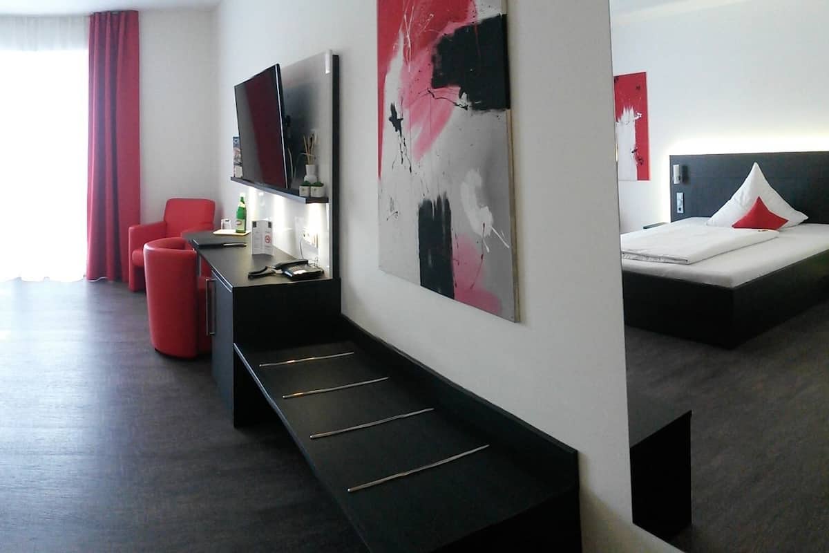 A modern hotel room with a large bed, a desk with a chair, a flat-screen TV, and a large abstract painting on the wall.