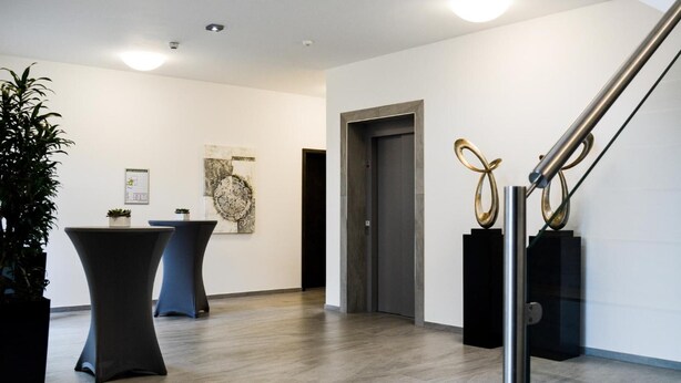 A modern interior with a wooden floor, a reception desk, a door, and a staircase with metal railings. - Campushotel GmbH (Hagen)