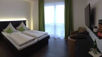 Ein Hotelzimmer mit Bett, Schreibtisch, Fernseher und einem Fenster mit Vorhängen.