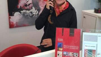 Una persona en un escritorio, con un cuadro abstracto rojo de fondo, una silla roja y un folleto rojo sobre el escritorio.