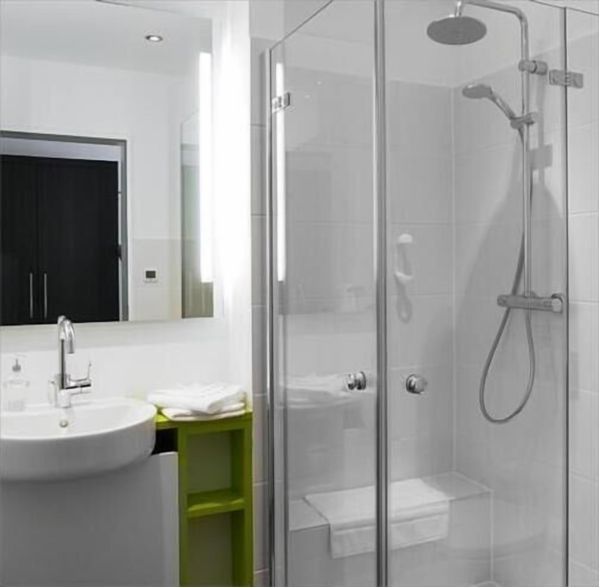 Ein modernes Badezimmer mit einer gläsernen Duschkabine, einem weißen Waschbecken und einem grünen Schrank.