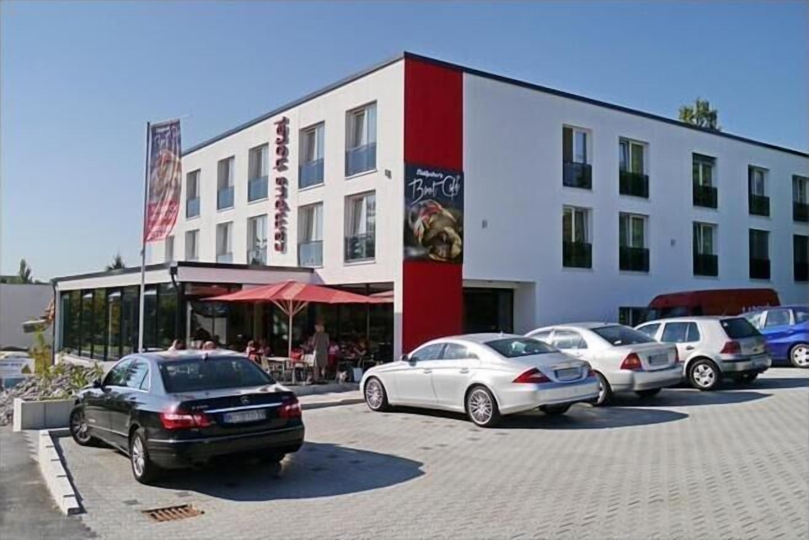Een modern gebouw met een gevel in rood en wit, een vlag en verschillende geparkeerde auto's ervoor.