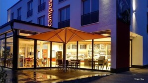 A hotel with a prominent 'Campus Hotel' sign, outdoor seating area with umbrellas, and a well-lit facade. - Campushotel GmbH (Hagen)
