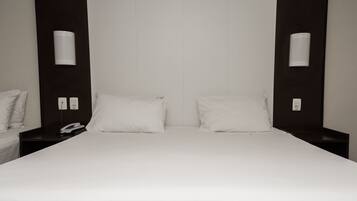 A hotel room with a large bed, two bedside tables, a phone, and wall-mounted light fixtures.