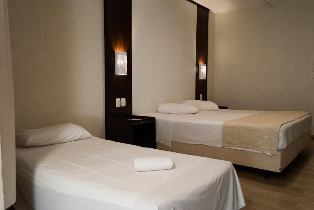 Ein Hotelzimmer mit zwei Einzelbetten, einem Nachttisch und Wandleuchten.