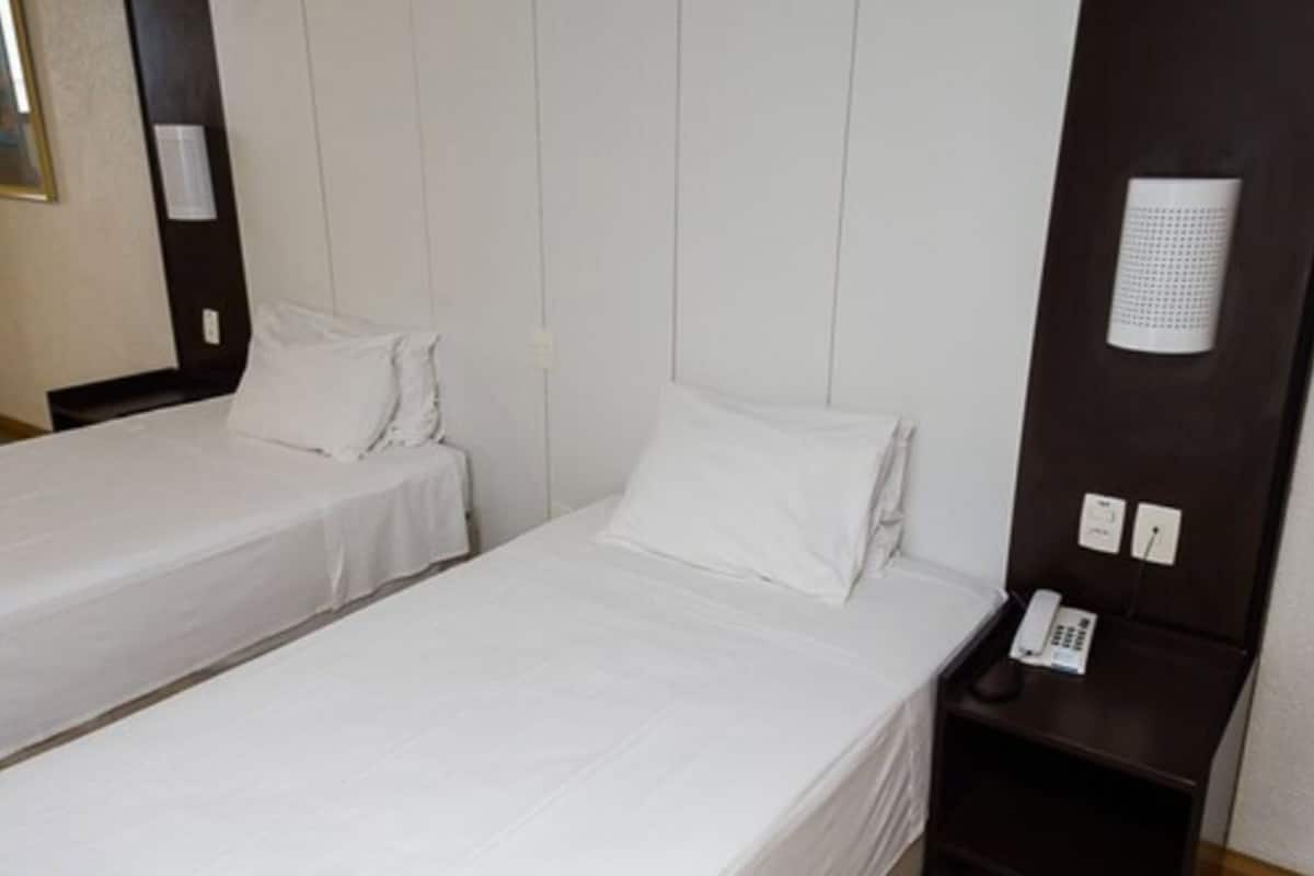 A hotel room with two single beds, a bedside table with a phone, and a wall-mounted light fixture.