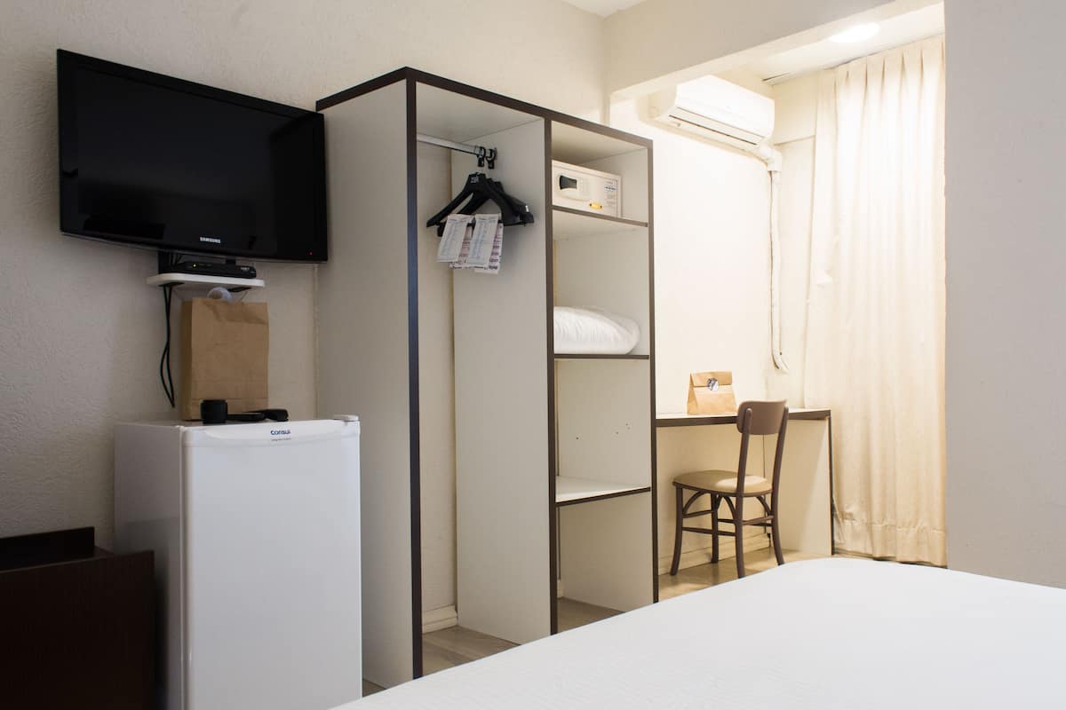 A hotel room with a bed, a desk, a chair, a television, a wardrobe, and a refrigerator.