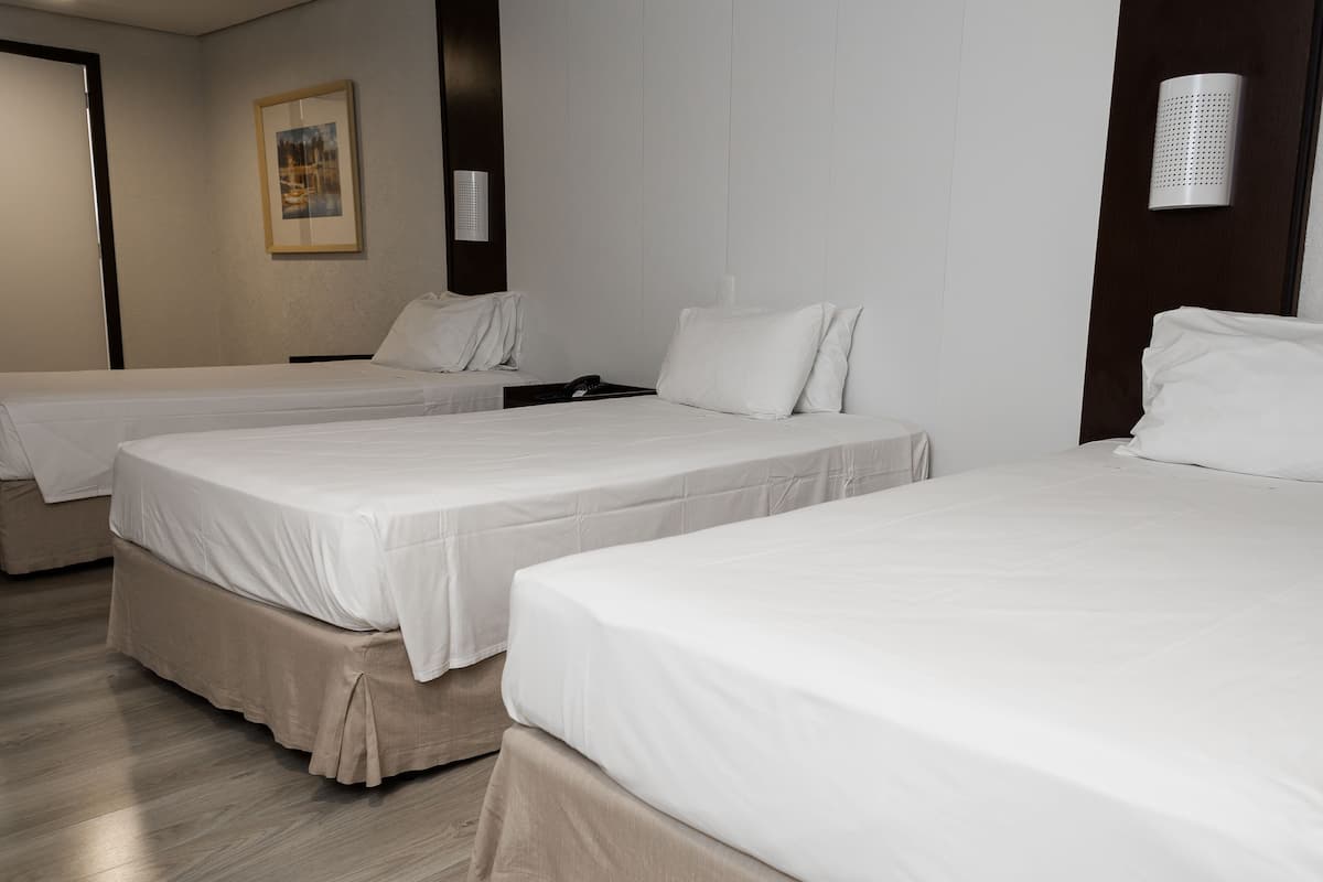 A hotel room with three single beds, a wooden floor, a framed picture on the wall, and a wall-mounted light fixture.