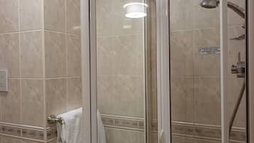 A glass-enclosed shower with a handheld showerhead, a towel rack with a towel, and a toilet paper holder.