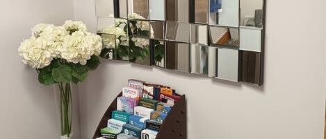 A wall with a mirrored panel and a small table with a vase of flowers and a magazine rack.