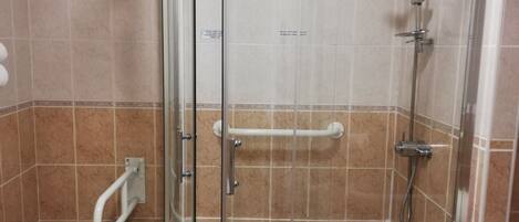 Ducha en esquina con puertas de vidrio, inodoro y silla blancos.