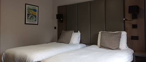 A hotel room with two beds, a headboard, a wall-mounted TV, and a framed picture.