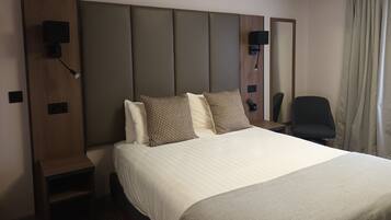 A hotel room with a large bed, a wooden headboard, a bedside table with a lamp, and a chair.