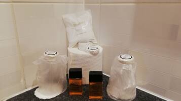 A bathroom corner with a shower cap, two bottles of Aqua Viva, and a white towel.