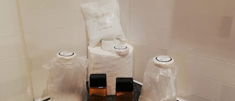 A bathroom corner with a shower cap, two bottles of Aqua Viva, and a white towel.