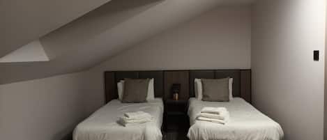 Een moderne hotelkamer met twee bedden, een klein nachtkastje met een lamp en een vloerbedekking.
