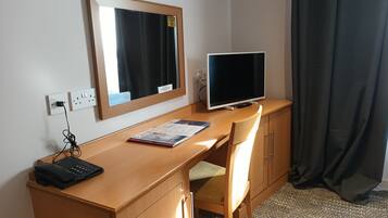 Una camera d'hotel con una scrivania in legno, un monitor computer, un telefono e una sedia.