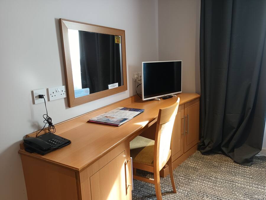 Una camera d'hotel con una scrivania in legno, un monitor computer, un telefono e una sedia.