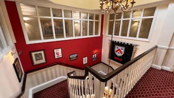 A grand staircase with a red carpet, white balustrades, and a chandelier.