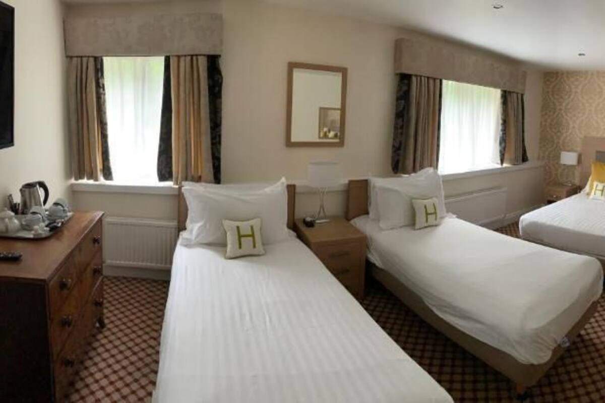 A hotel room with two beds, a desk, a chair, and a small table.
