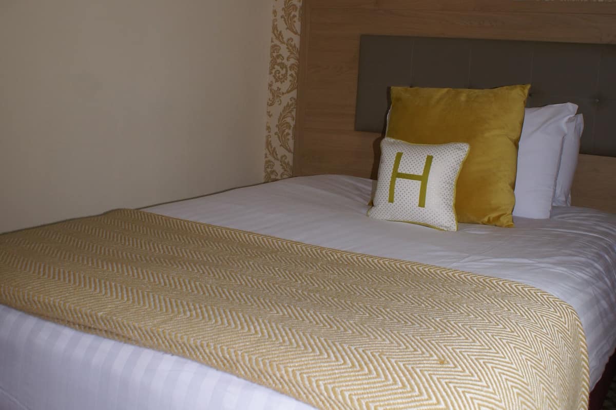 A hotel room with a large bed, a headboard, a framed picture on the wall, and patterned wallpaper.