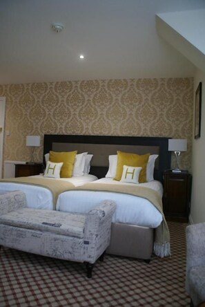 A hotel room with a large bed, two bedside tables, a chair, and a patterned carpet. - Haley's Hotel (Leeds)