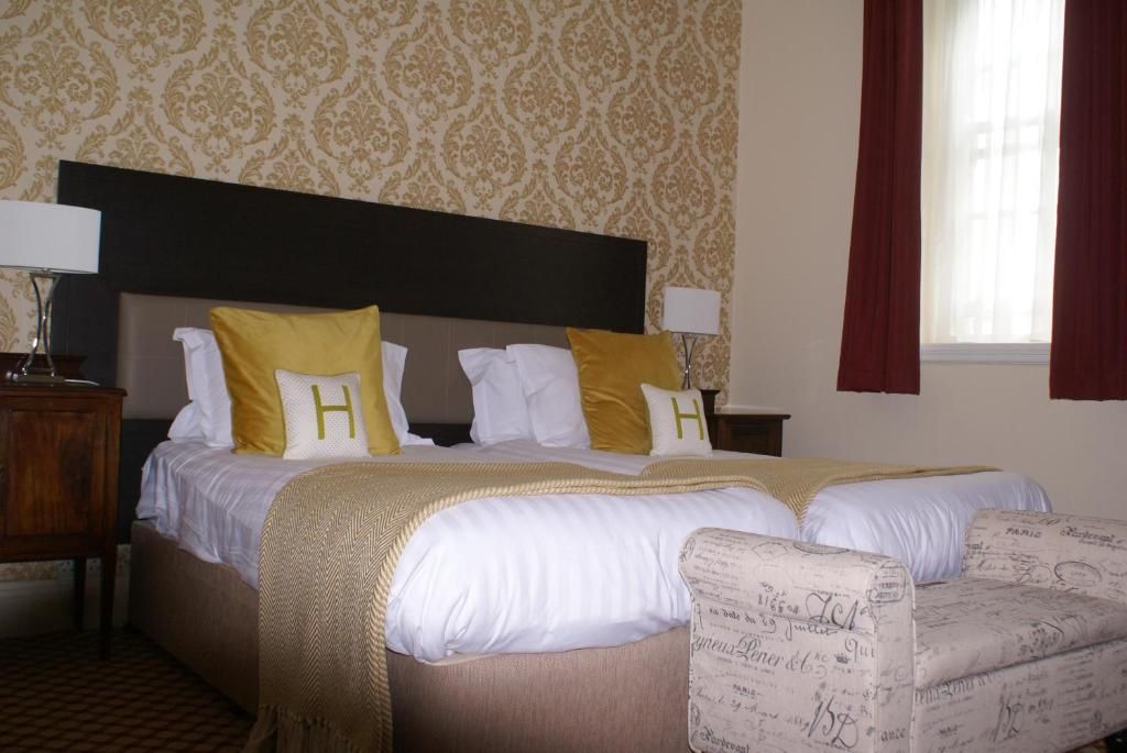 A hotel room with a double bed, two nightstands, a bedside table, and a window with curtains.