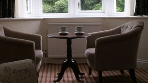 A room with two armchairs, a small table with cups, and a window with curtains. - Haley's Hotel (Leeds)