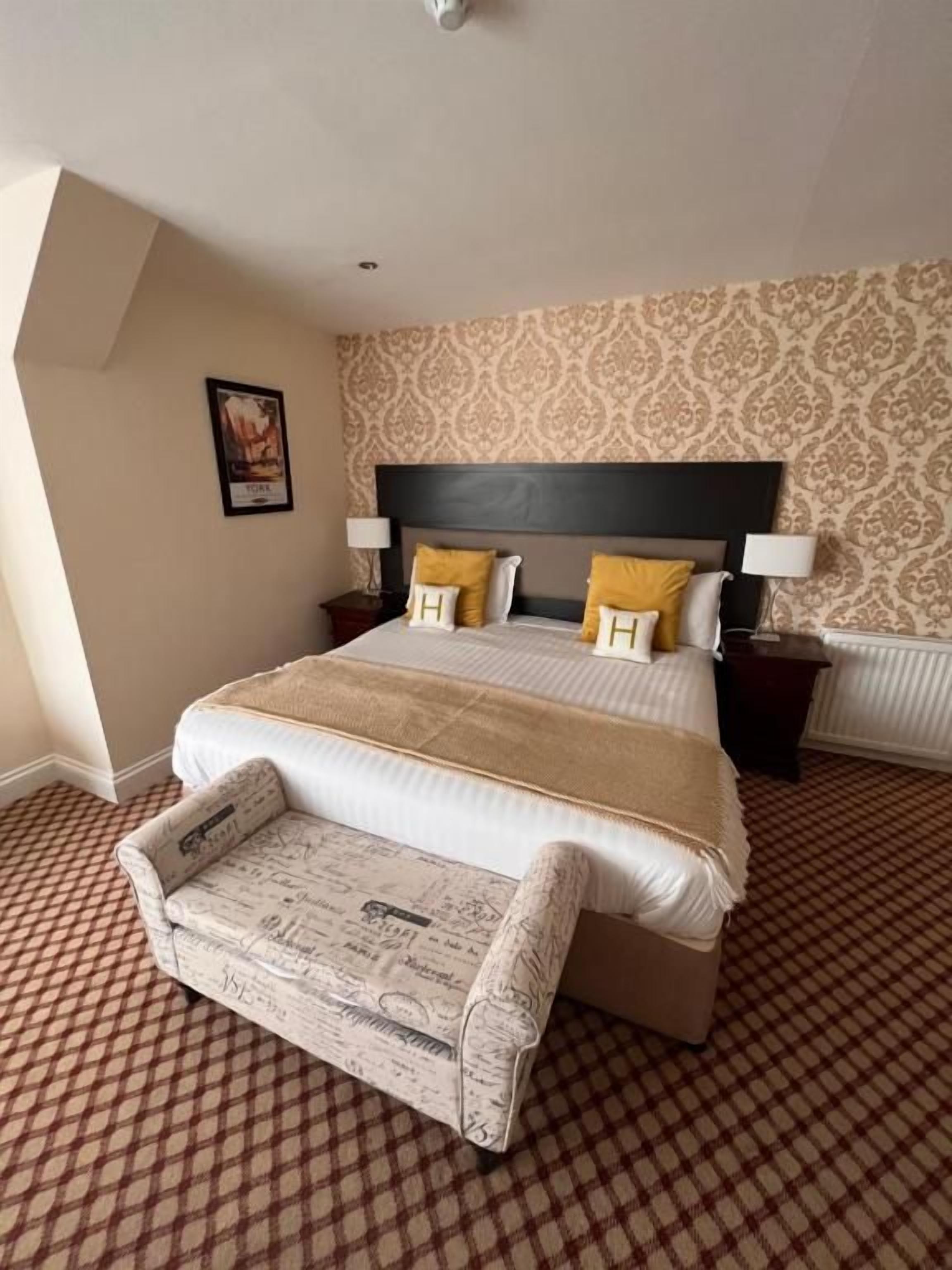 A hotel room with a large bed, a bedside table, a chair, and a patterned carpet.