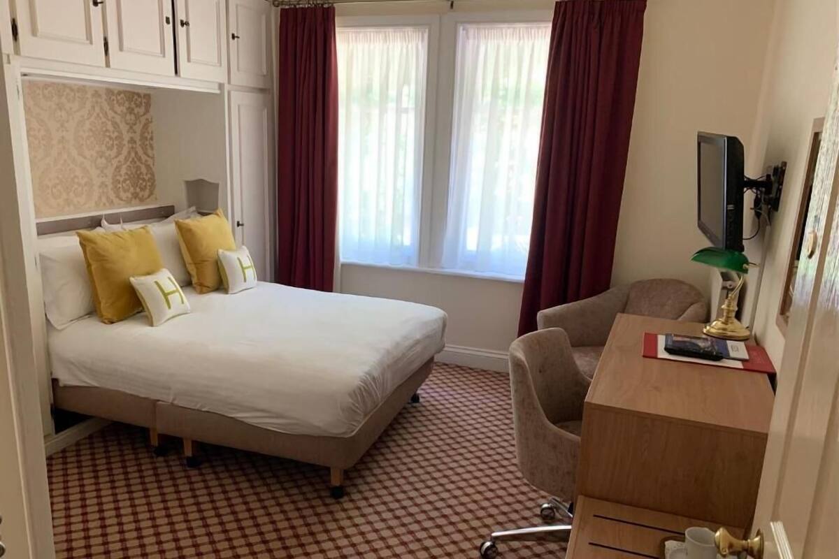 A hotel room with a bed, a desk, a chair, a television, and a window with curtains.