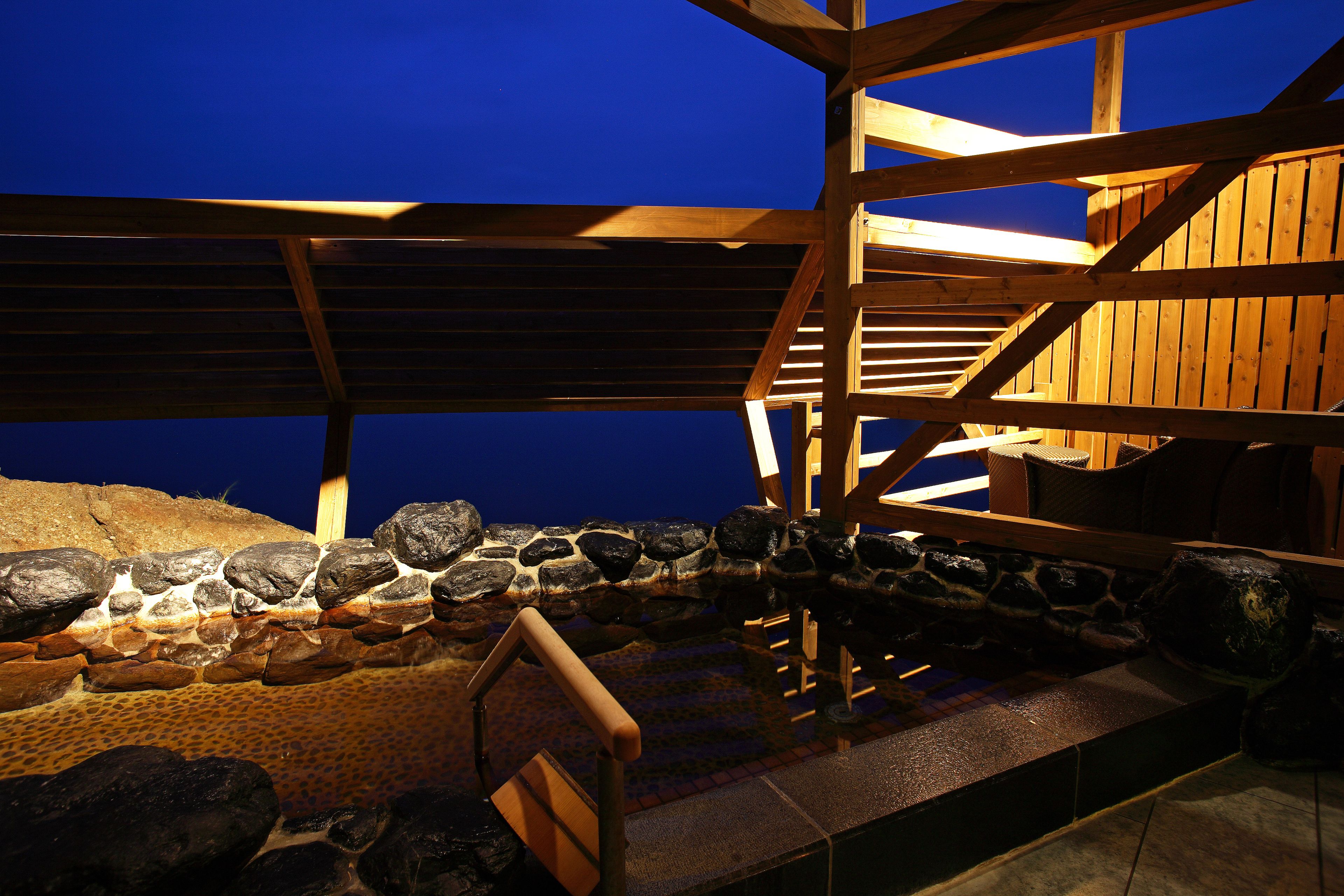 A wooden deck with a stone wall and a wooden railing.