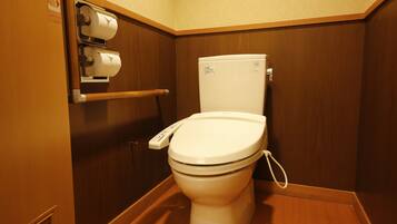 A small, compact bathroom with a white toilet, a hand dryer, and a paper towel dispenser.