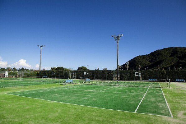 A tennis court with multiple courts, floodlights, and seating areas.