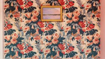 Une salle de bain avec un papier peint à motifs floraux, un tableau encadré et une baignoire blanche.