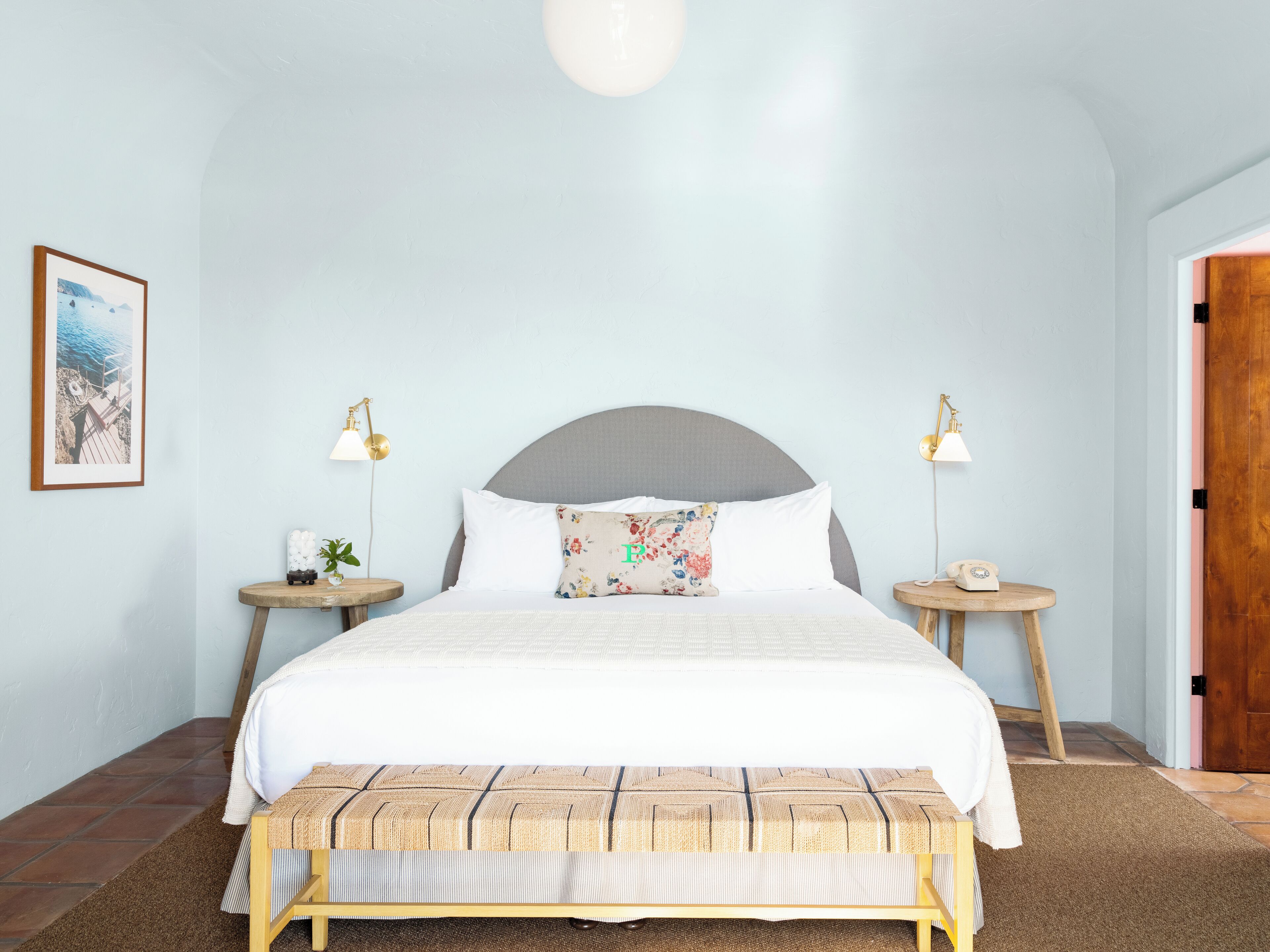 A bedroom with a bed, two bedside tables, a nightstand, a bench, a framed picture, and a door.