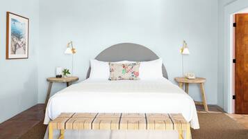 A bedroom with a bed, two bedside tables, a nightstand, a bench, a framed picture, and a door.