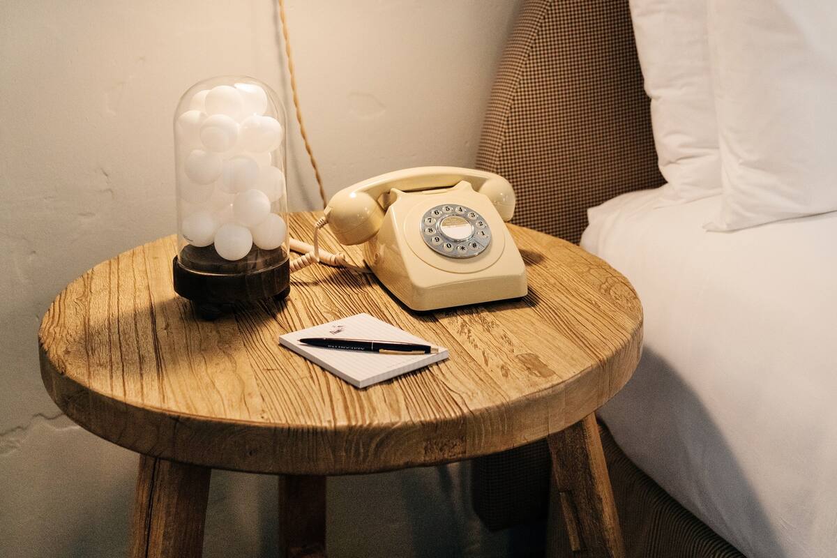 Ein Nachttisch aus Holz mit einem alten Telefon, einer Lampe und einer Glasdekoration.