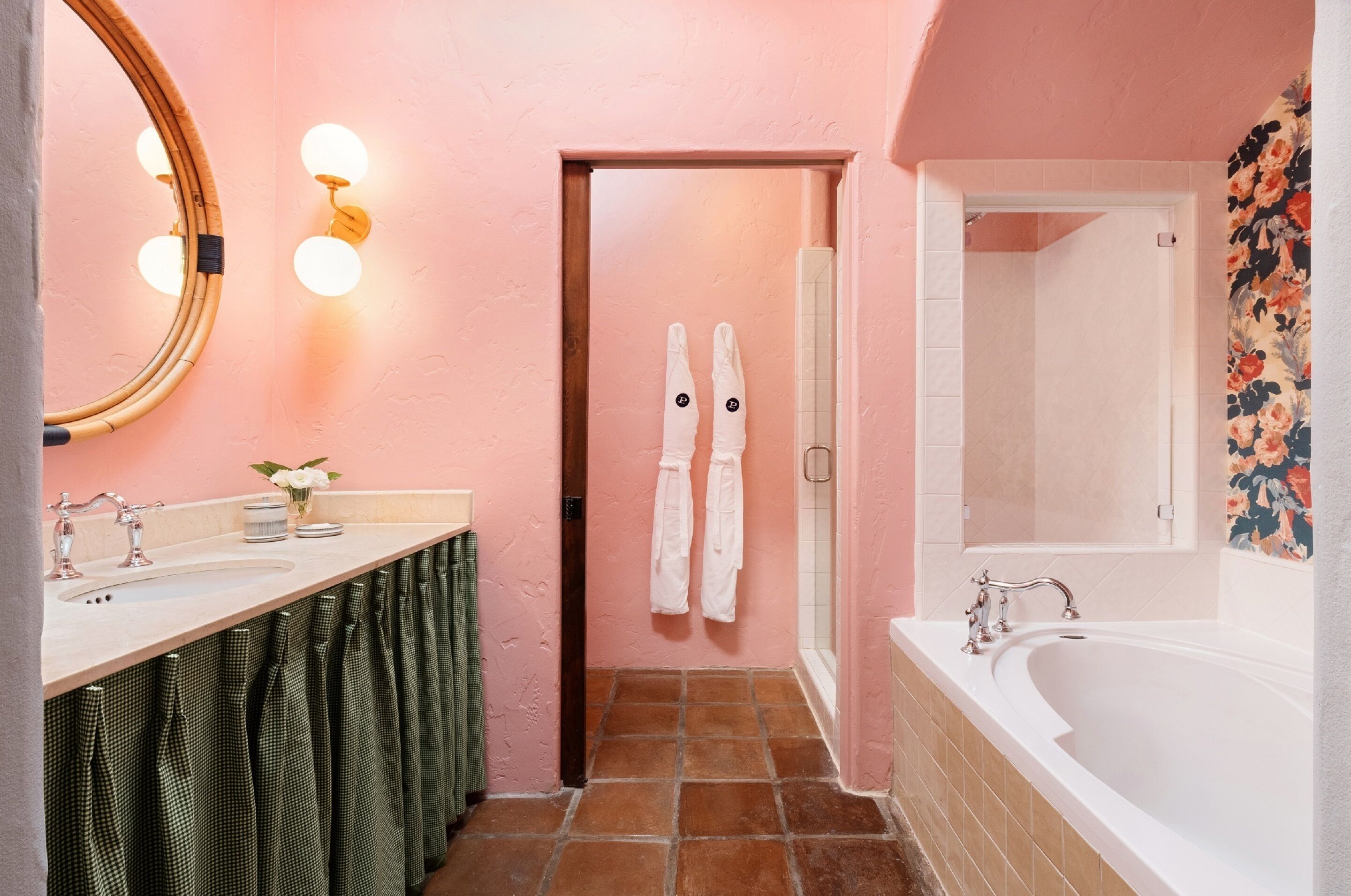 A bathroom with a pink wall, a large mirror, a sink, a bathtub, and a shower.