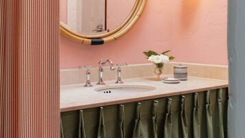 A bathroom with a round mirror, two wall-mounted lights, a sink, and a towel rack.