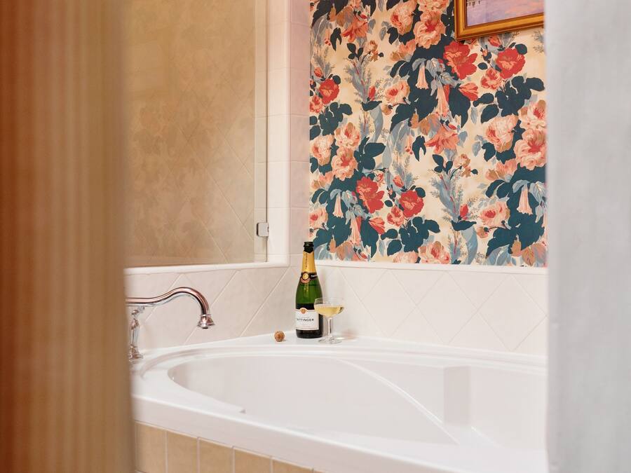 A bathroom with a bathtub, a bottle of champagne, and a glass of champagne on the edge of the tub.