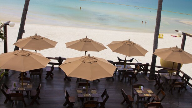 A beachside restaurant with outdoor seating and umbrellas, overlooking a clear blue sea. - Tommy Resort (Ko Pha-ngan)