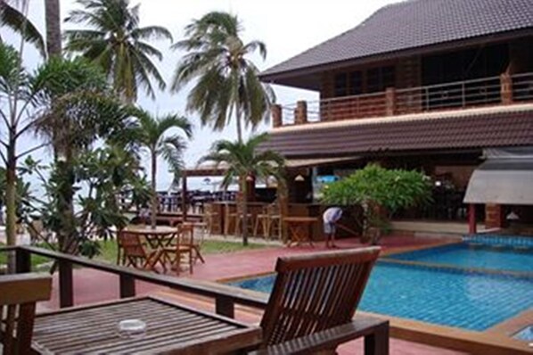 A poolside area with wooden furniture, a pool, and palm trees.