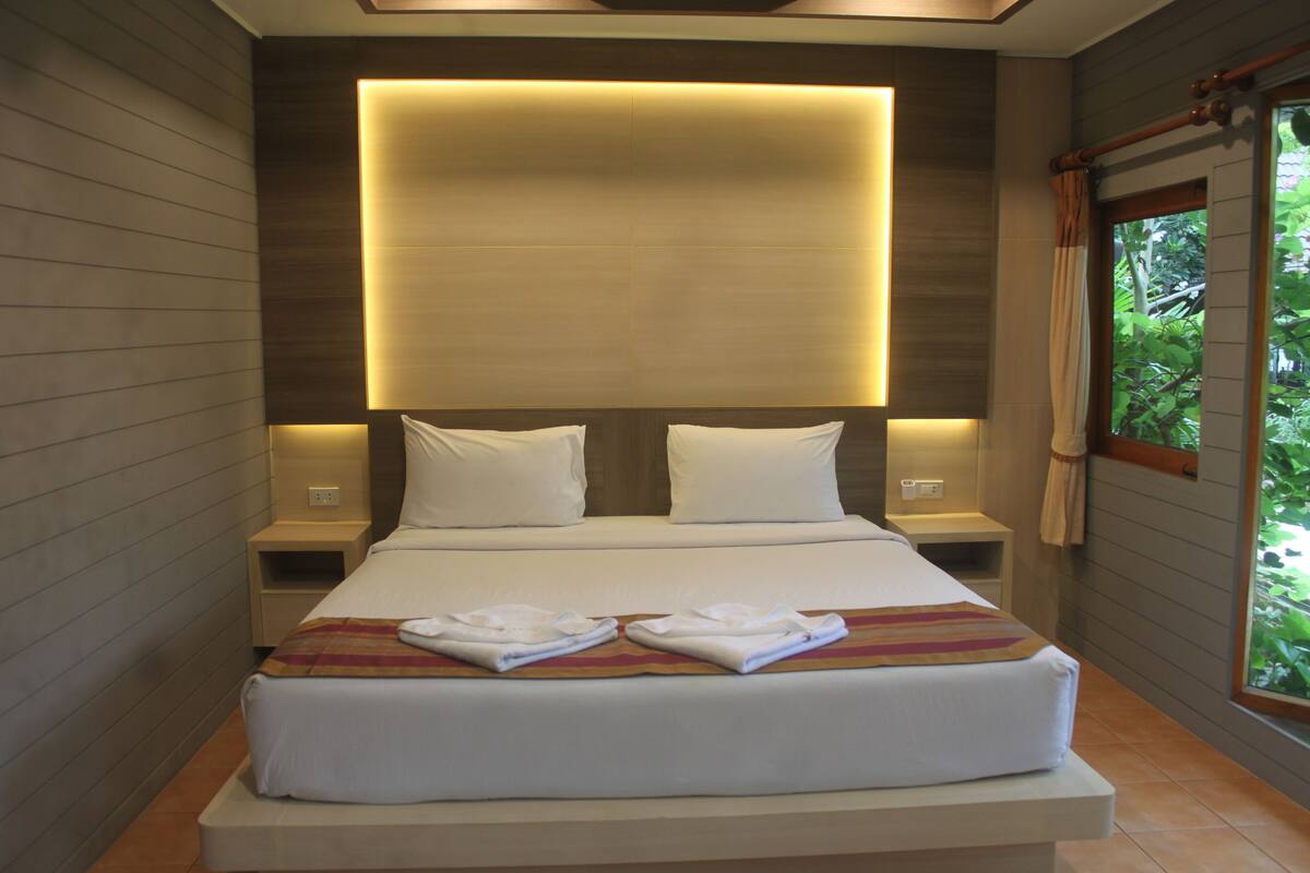 Una habitación de hotel moderna con una cama grande, dos mesitas de noche y vistas a zonas verdes a través de una ventana.