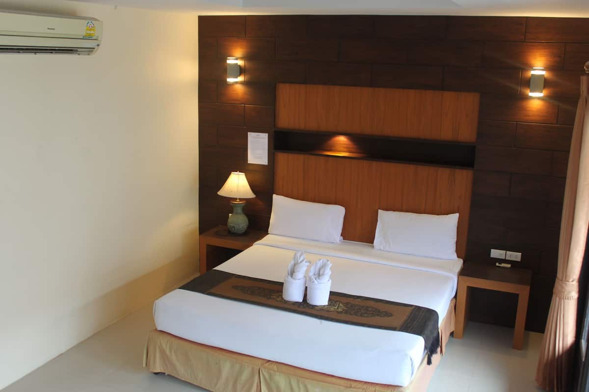 Habitación de hotel con cabecera de madera, cama con sábanas blancas, dos mesitas de noche con lámparas y un par de toallas sobre la cama.
