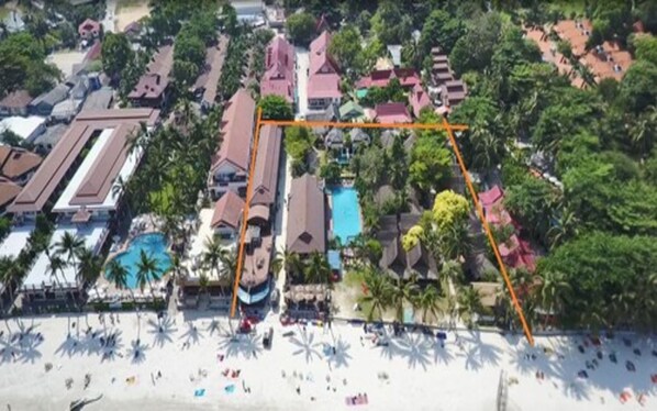 An aerial view of a resort with multiple buildings, a swimming pool, and a beach area with umbrellas. - Tommy Resort (Ko Pha-ngan)